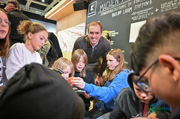 菲利普·拉姆在柏林国际绿色周现场与孩子们交流健康饮食，背景是一块大黑板。