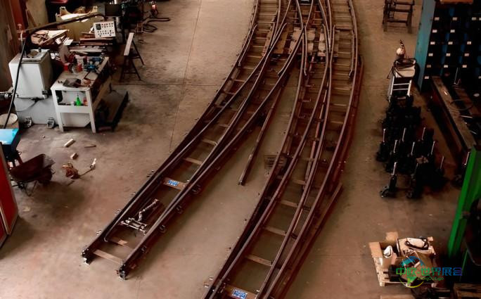 俯瞰大型工业厂房内部，可见多组平行轨道及沿墙排列的工作台